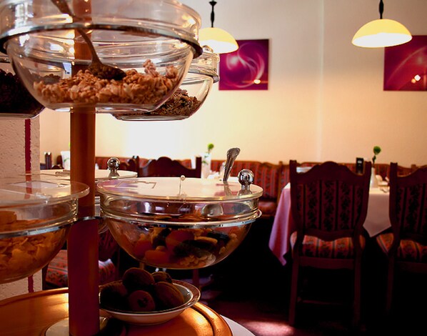 Ein reichhaltiges Buffet mit verschiedenen Speisen in Glasbehältern, vor einer Gaststätteneinrichtung mit Stühlen und Tischen.