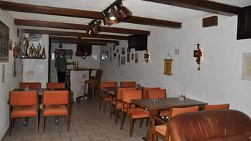 Zona pranzo con tavoli in legno e sedie arancioni, zona bar con bancone, e una persona in piedi vicino all'ingresso.