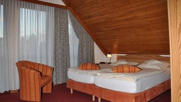Een slaapkamer met een houten plafond, een bed met veel kussens, een stoel en een lamp.