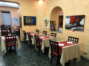 A restaurant with tables covered in red and white tablecloths, black chairs, and artwork on the walls. - Hotel San Remo (Rome)