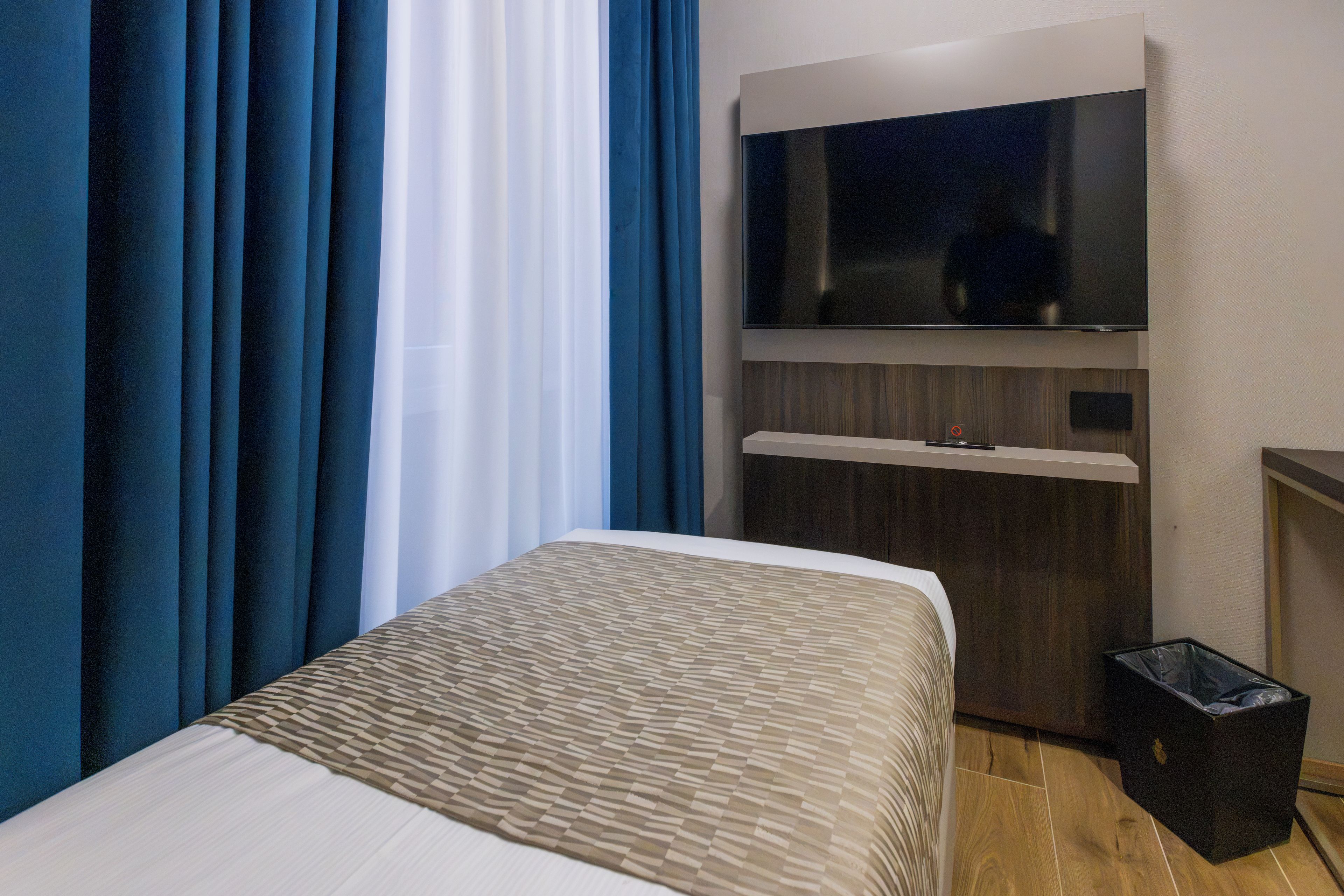 A hotel room with a bed, a TV mounted on the wall, and a trash bin.