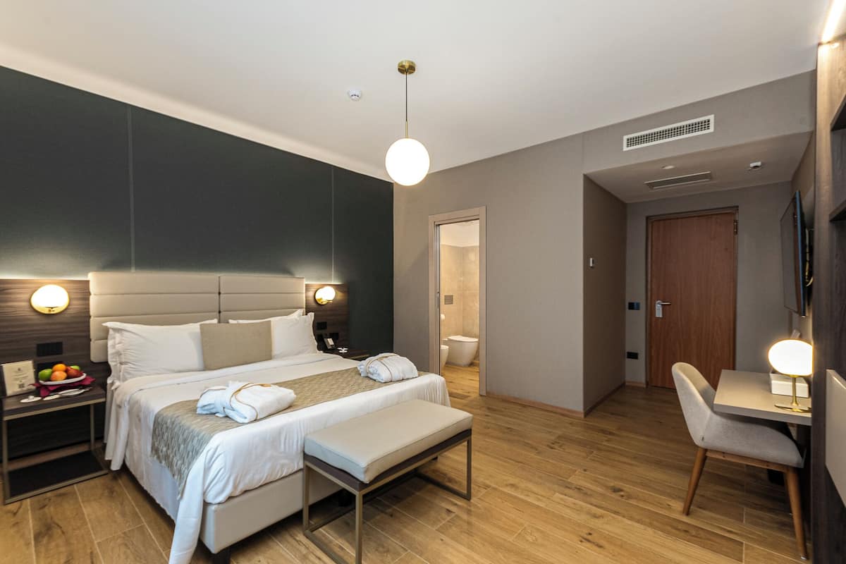 A modern hotel room with a large bed, bedside tables, a desk, and a chair.