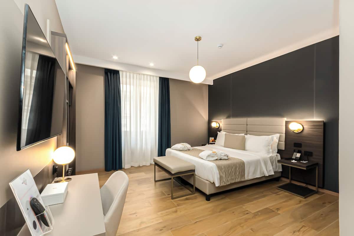 A modern hotel room with a bed, bedside tables, a desk, and a TV.