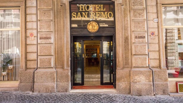 The entrance of Hotel San Remo with a classic stone facade, a prominent entrance door, and a sign above the door. - Hotel San Remo (Rome)