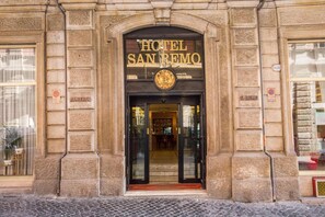 La entrada del Hotel San Remo, con una fachada clásica de piedra, una puerta principal destacada y un cartel sobre la puerta.