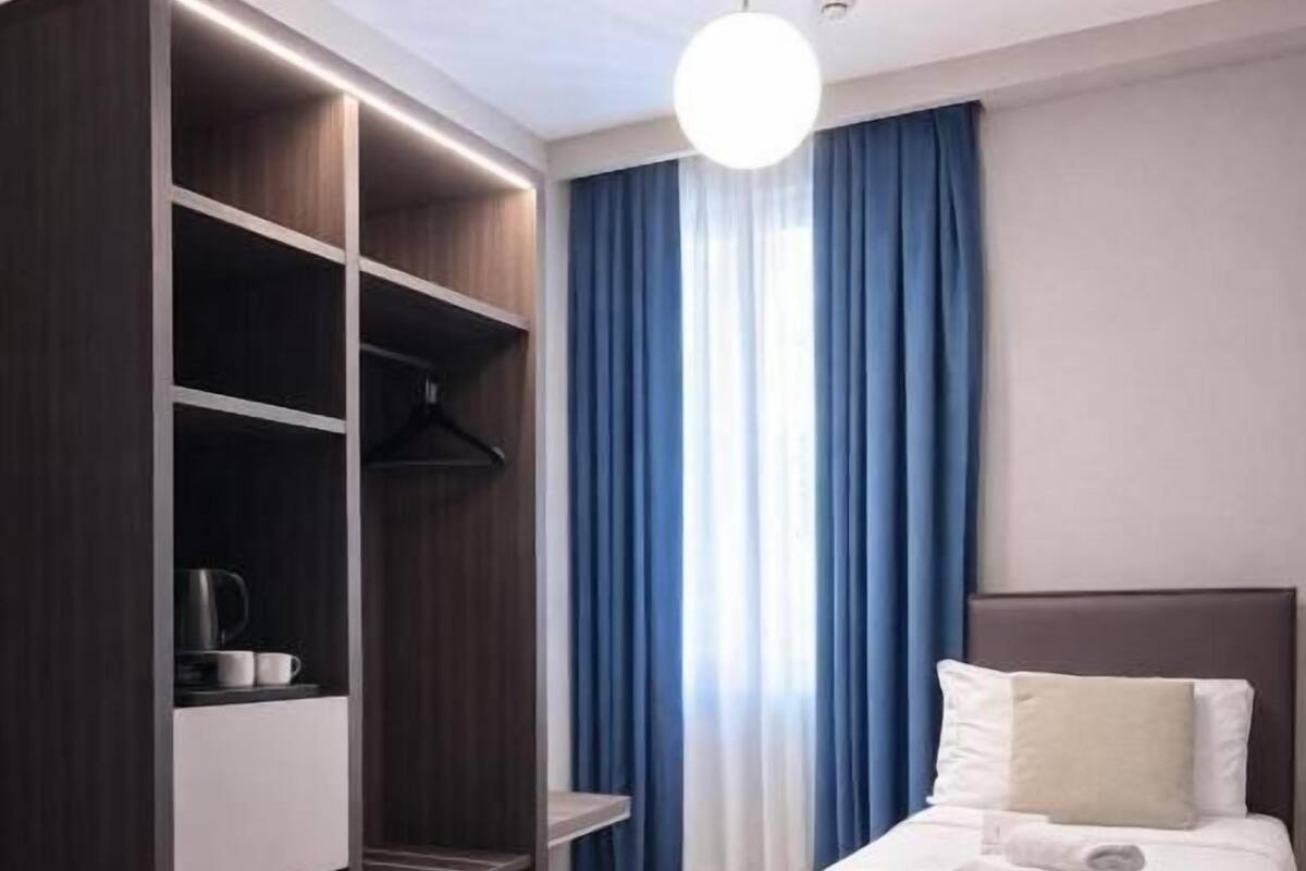 A hotel room with a bed, a wardrobe, and a window with curtains.