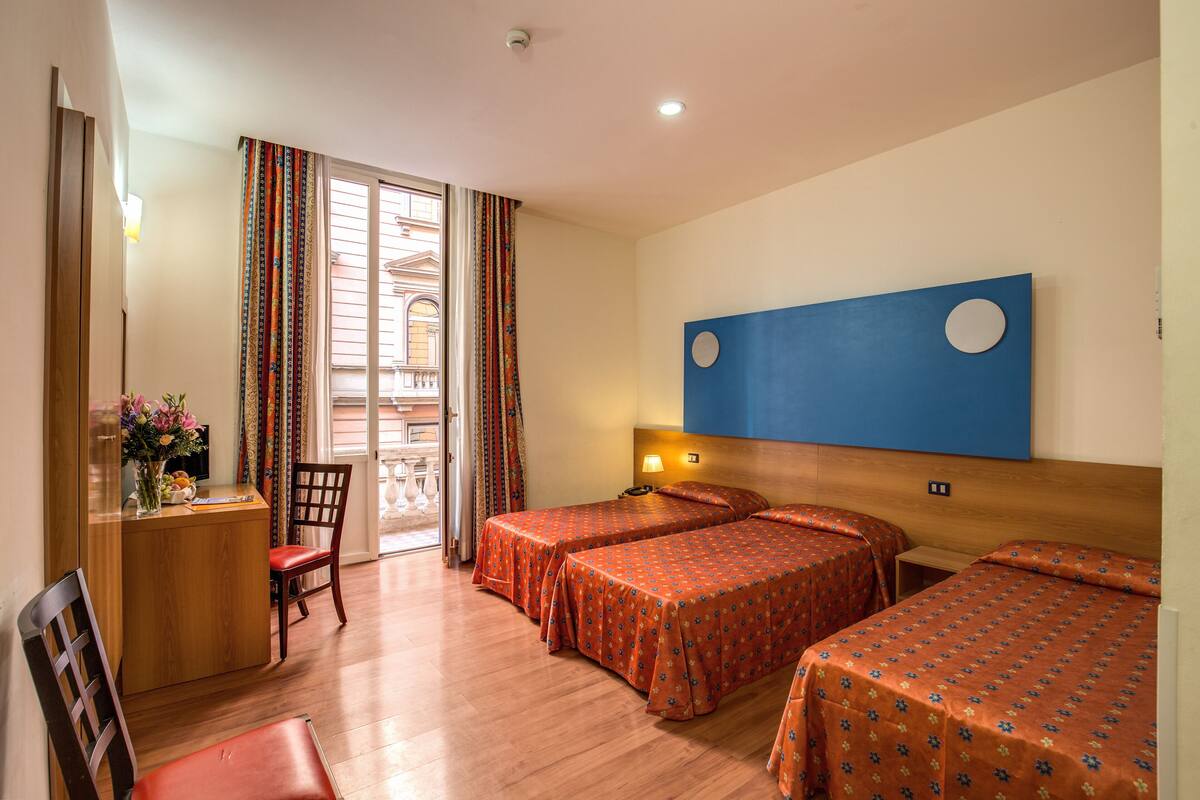 A hotel room with two beds, a desk with a chair, a TV, and a window with curtains.