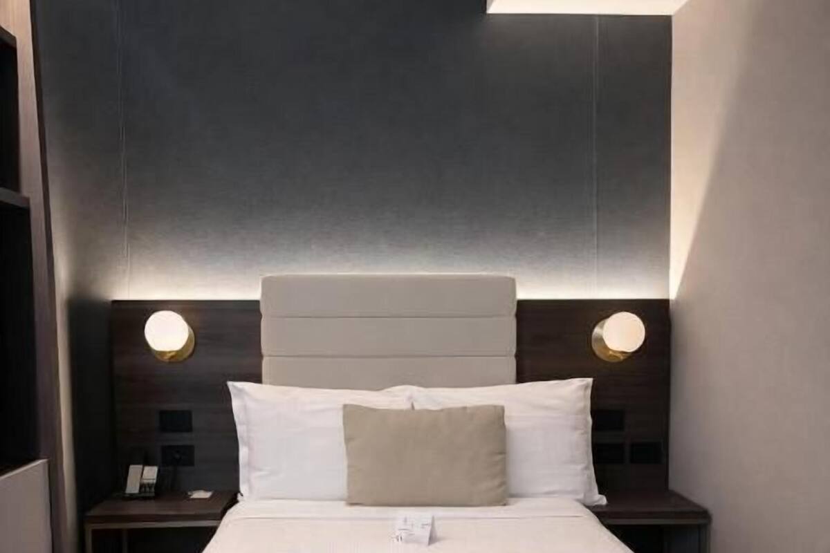 A modern hotel room with a large bed, bedside tables, a bench, and wall-mounted lighting.