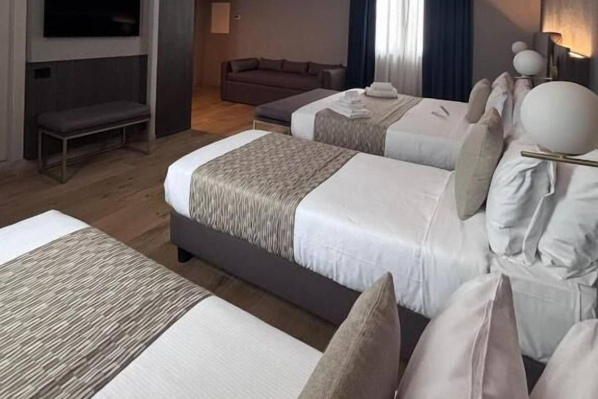 A hotel room with two beds, a sofa, a TV, and a desk.