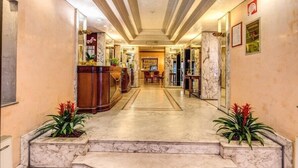 A hotel lobby with marble flooring, a reception desk, and a dining area in the background. - Hotel San Remo (Rome)