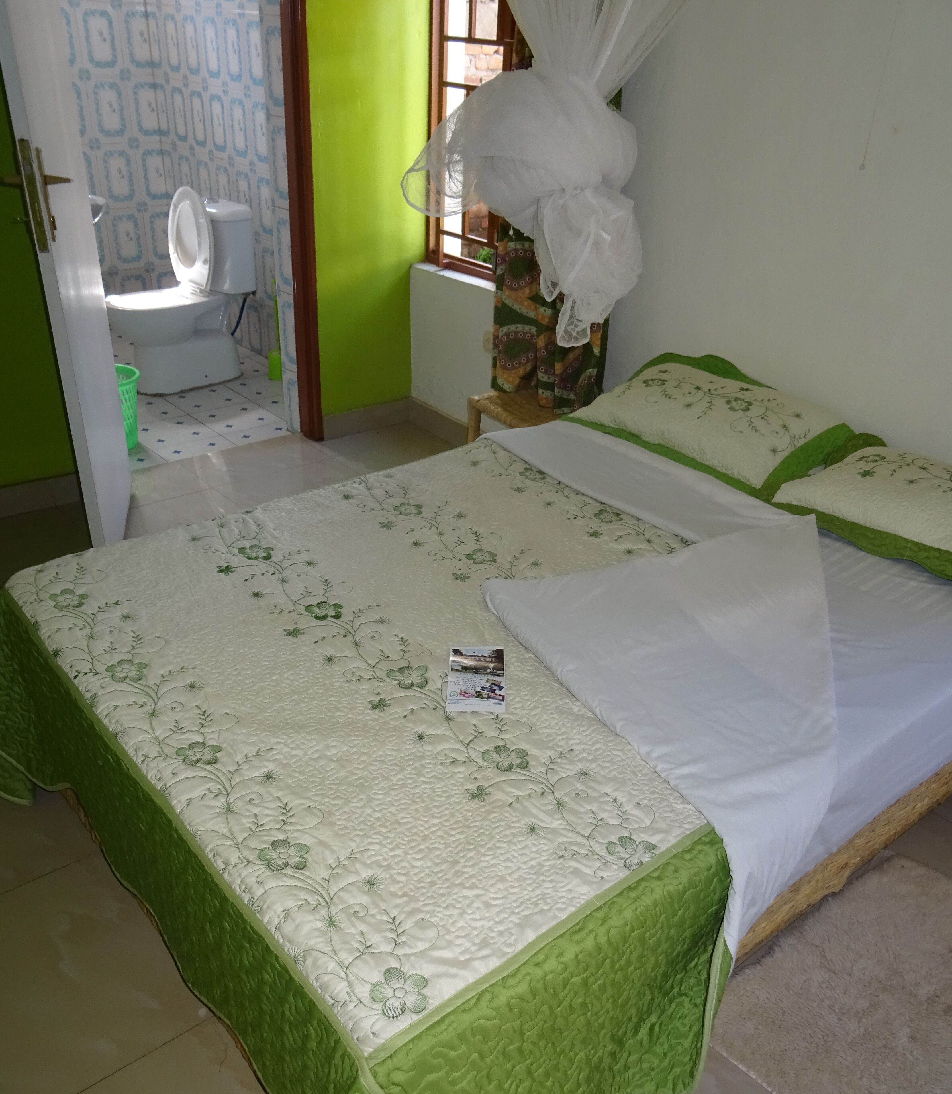 A room with two beds, a green door, a white toilet, and a window with a curtain.