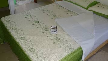 A room with two beds, a green door, a white toilet, and a window with a curtain.
