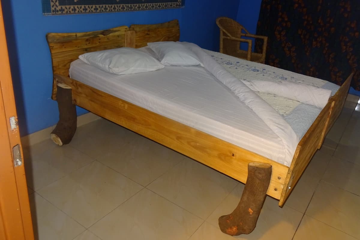 Ein Bett mit Holzbettgestell und weißer Bettwäsche, ein Stuhl und ein gemusterter Vorhang in einem Zimmer mit blauen Wänden.