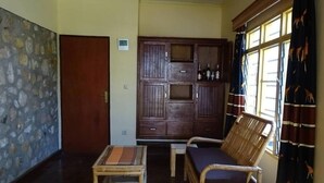 Una habitación con piso de madera, pared de piedra, un armario de madera con botellas, un sofá y una ventana con cortinas.