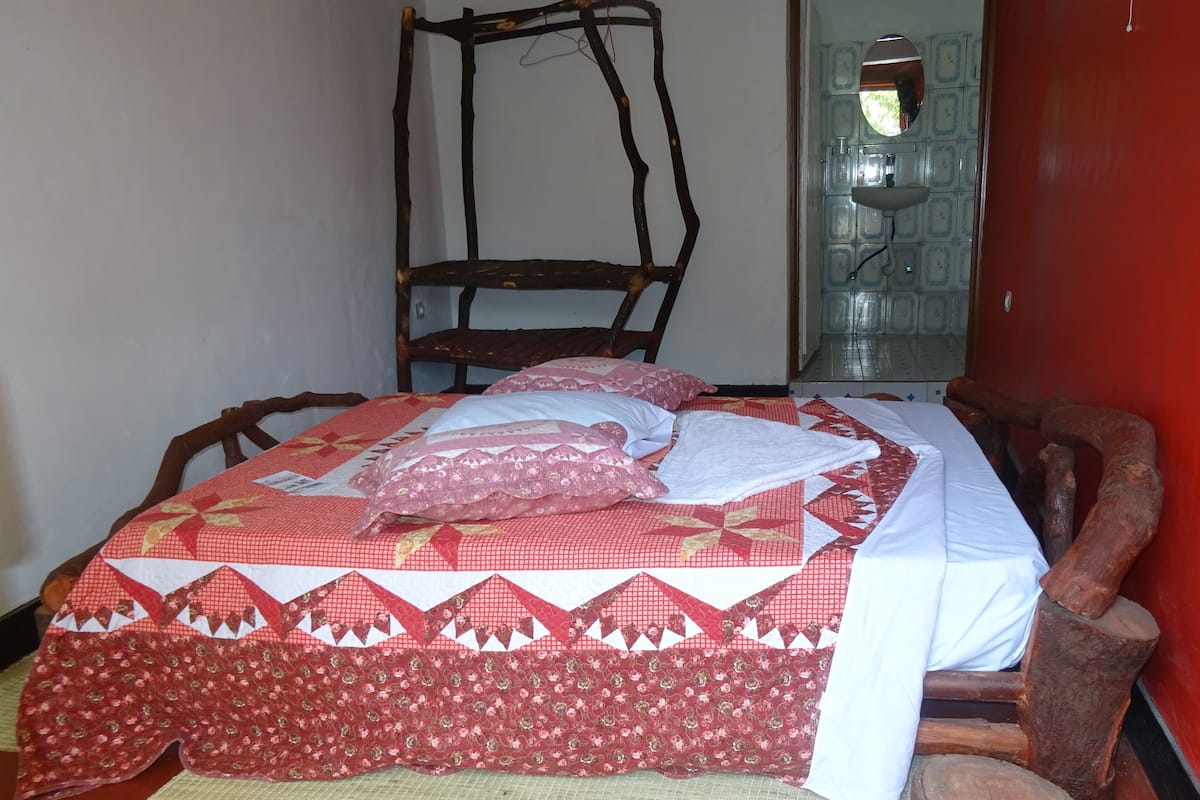 Ein Bett mit einer rot-weißen Musterdecke, ein Holzstuhl und ein rustikales Holz-Kopfende.