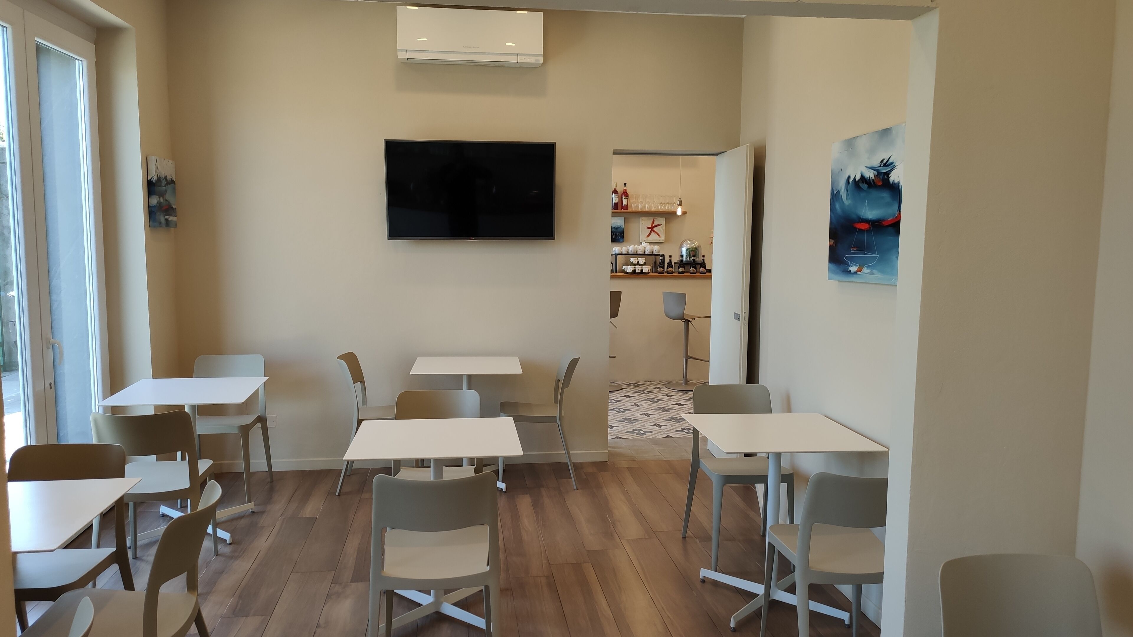A modern room with white tables and chairs, a flat-screen TV, and a painting on the wall.