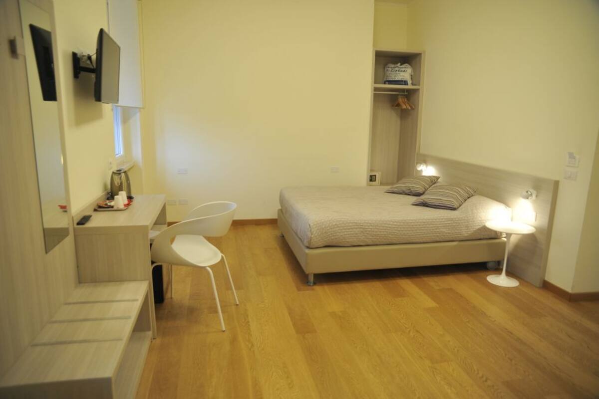 Un dormitorio con cama, mesita de noche, silla y escritorio con otra silla.