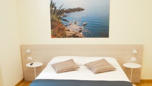 Un dormitorio moderno con una cama grande, dos mesitas de noche, un cuadro colgado en la pared con una escena costera y suelo de madera.