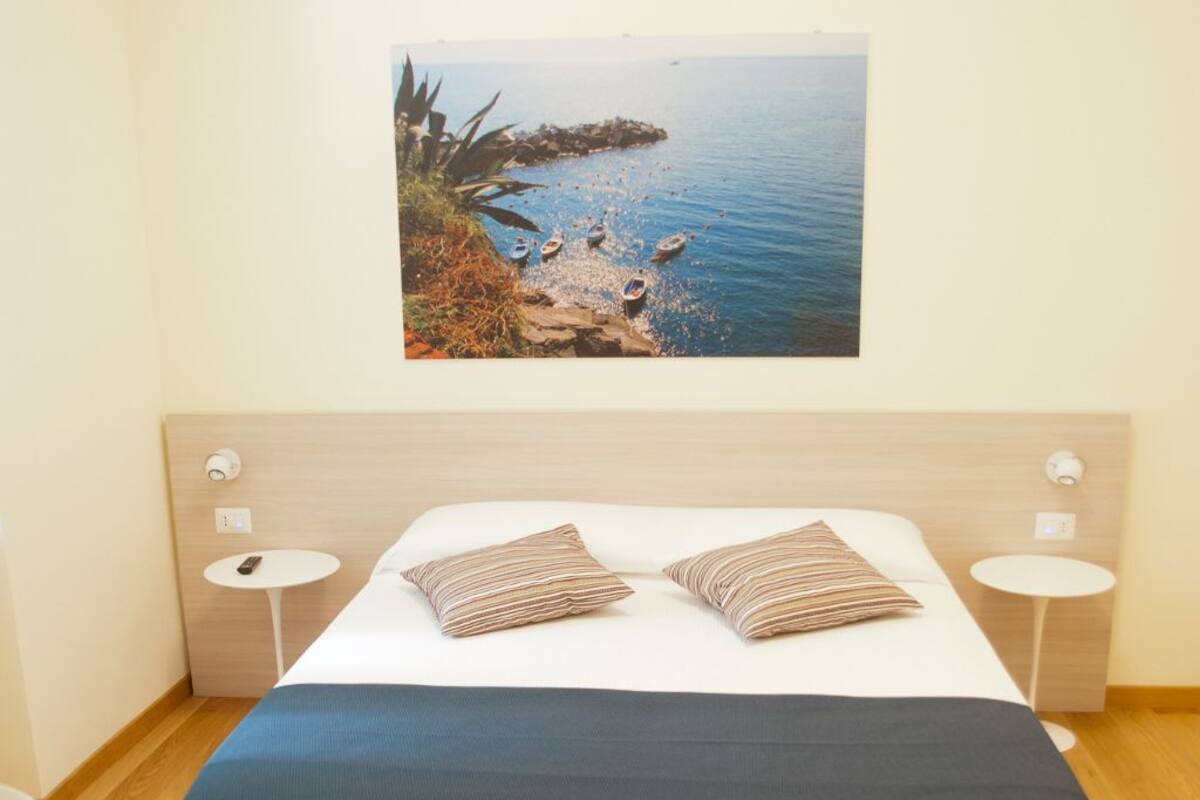 Un dormitorio moderno con una cama grande, dos mesitas de noche, un cuadro colgado en la pared con una escena costera y suelo de madera.