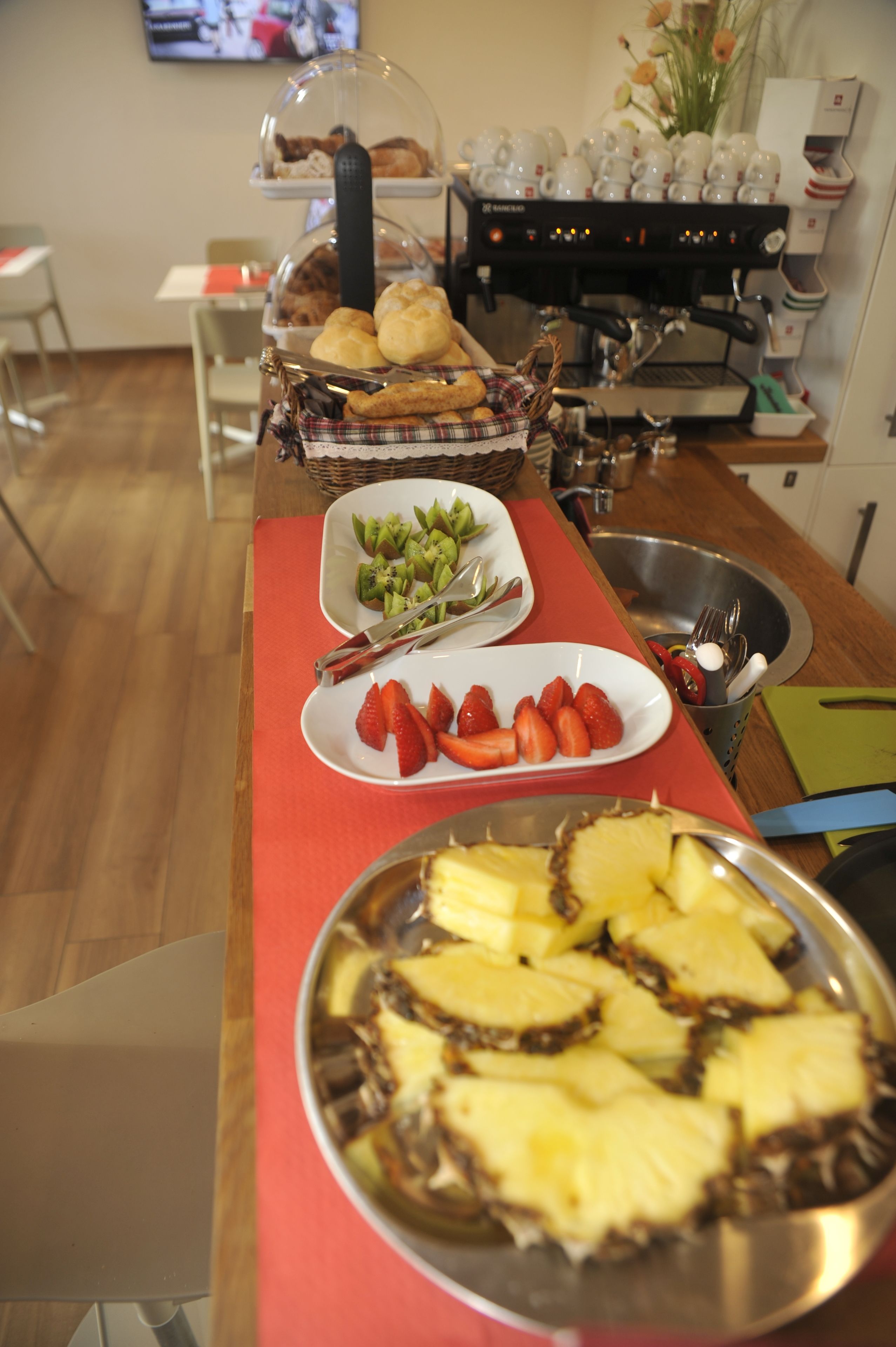 A buffet table with various food items including fruits, pastries, and a coffee machine.