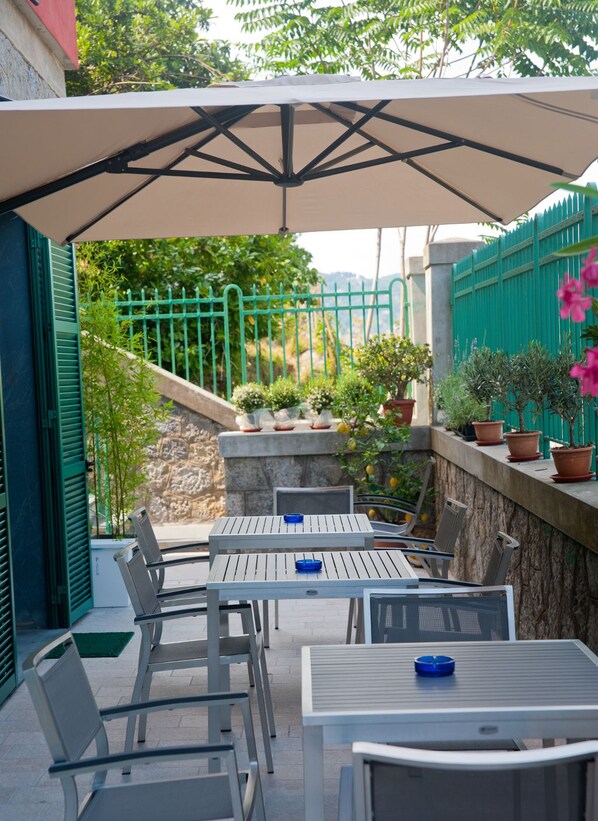An outdoor patio with tables and chairs, a green fence, and potted plants.