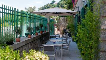 Une terrasse extérieure avec une table et des chaises, entourée de plantes en pot et d’une clôture verte.