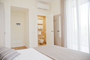 Una habitación de hotel con cama, baño visible a través de una puerta abierta y ventana con cortinas.