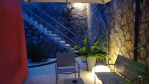 Un área de estar al aire libre con un muro de piedra de fondo, una escalera y plantas en macetas.