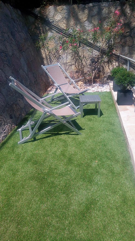 A backyard with artificial grass, two lounge chairs, a small table, and a potted plant.