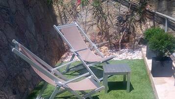 A backyard with artificial grass, two lounge chairs, a small table, and a potted plant.