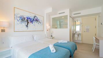 Habitación de hotel con dos camas, un cuadro abstracto grande, un escritorio y un baño visible a través de una puerta abierta.