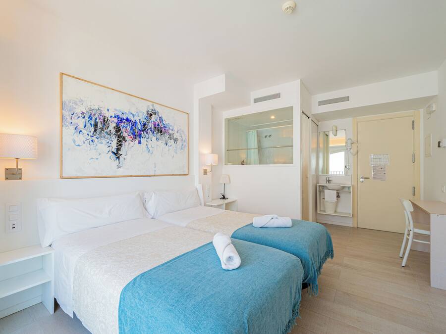 Habitación de hotel con dos camas, un cuadro abstracto grande, un escritorio y un baño visible a través de una puerta abierta.