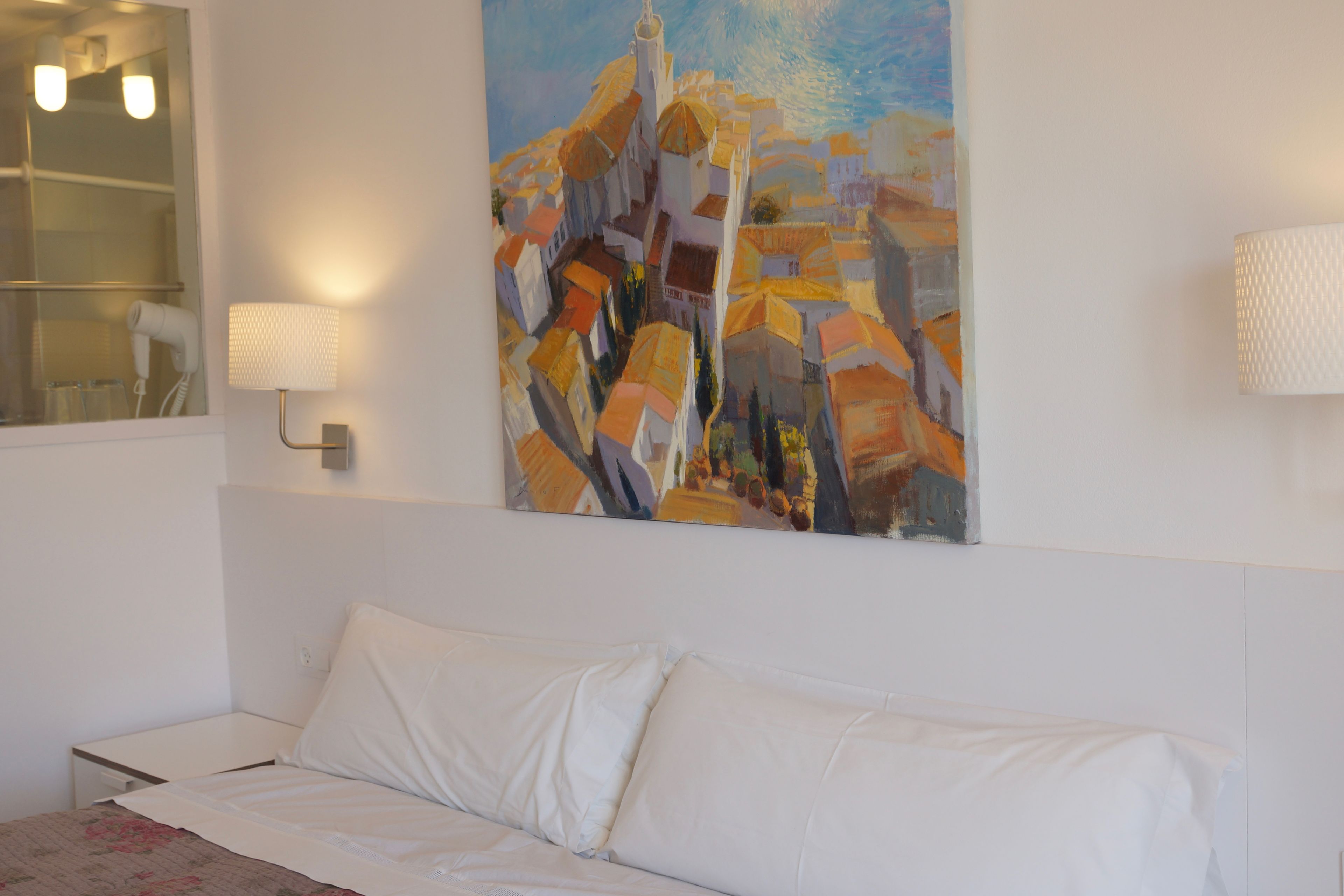 A hotel room with a bed, a painting on the wall, and a lamp.