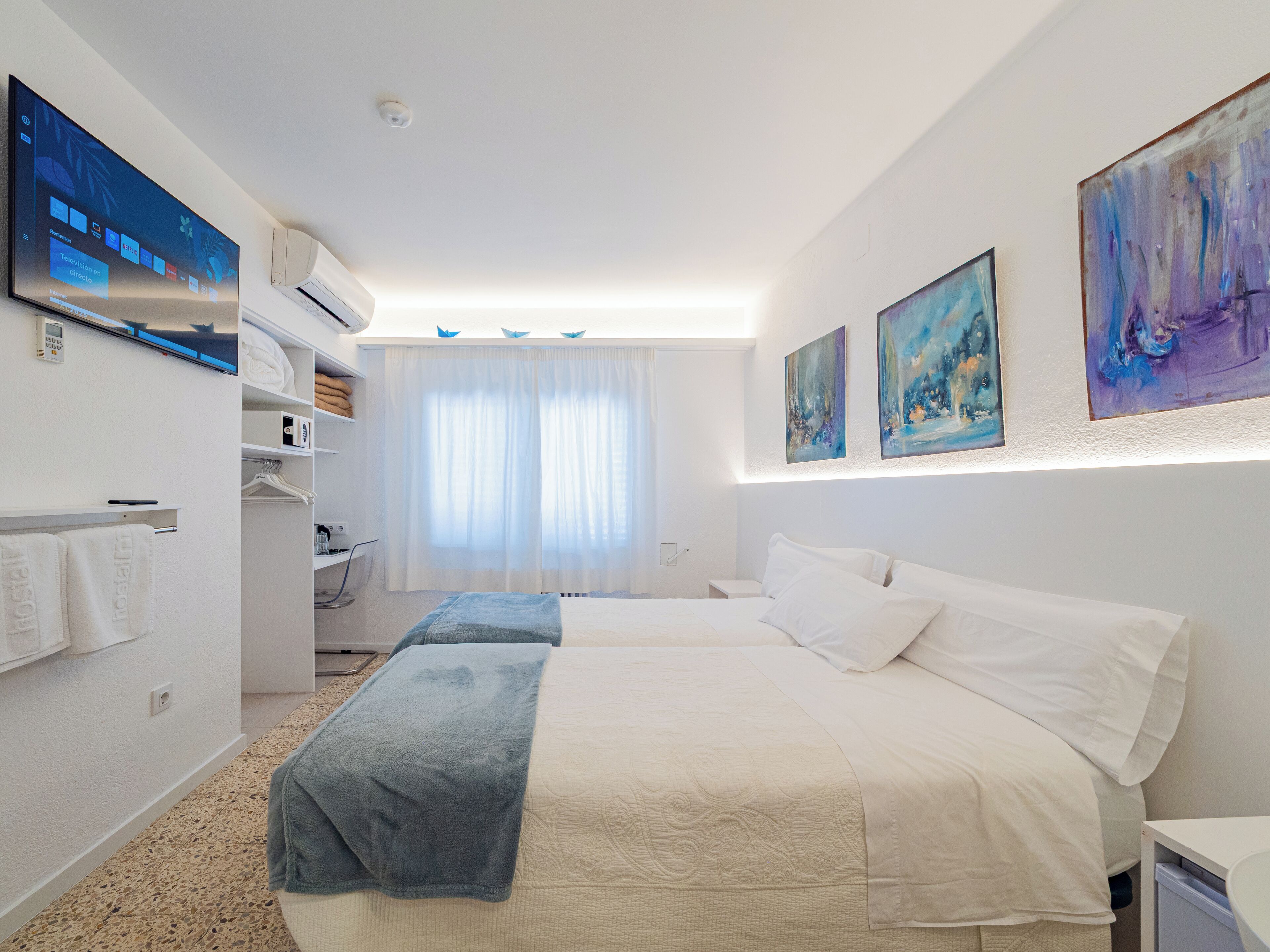 Une chambre d’hôtel avec un lit, un bureau, une chaise, une télévision et des œuvres d’art accrochées aux murs.