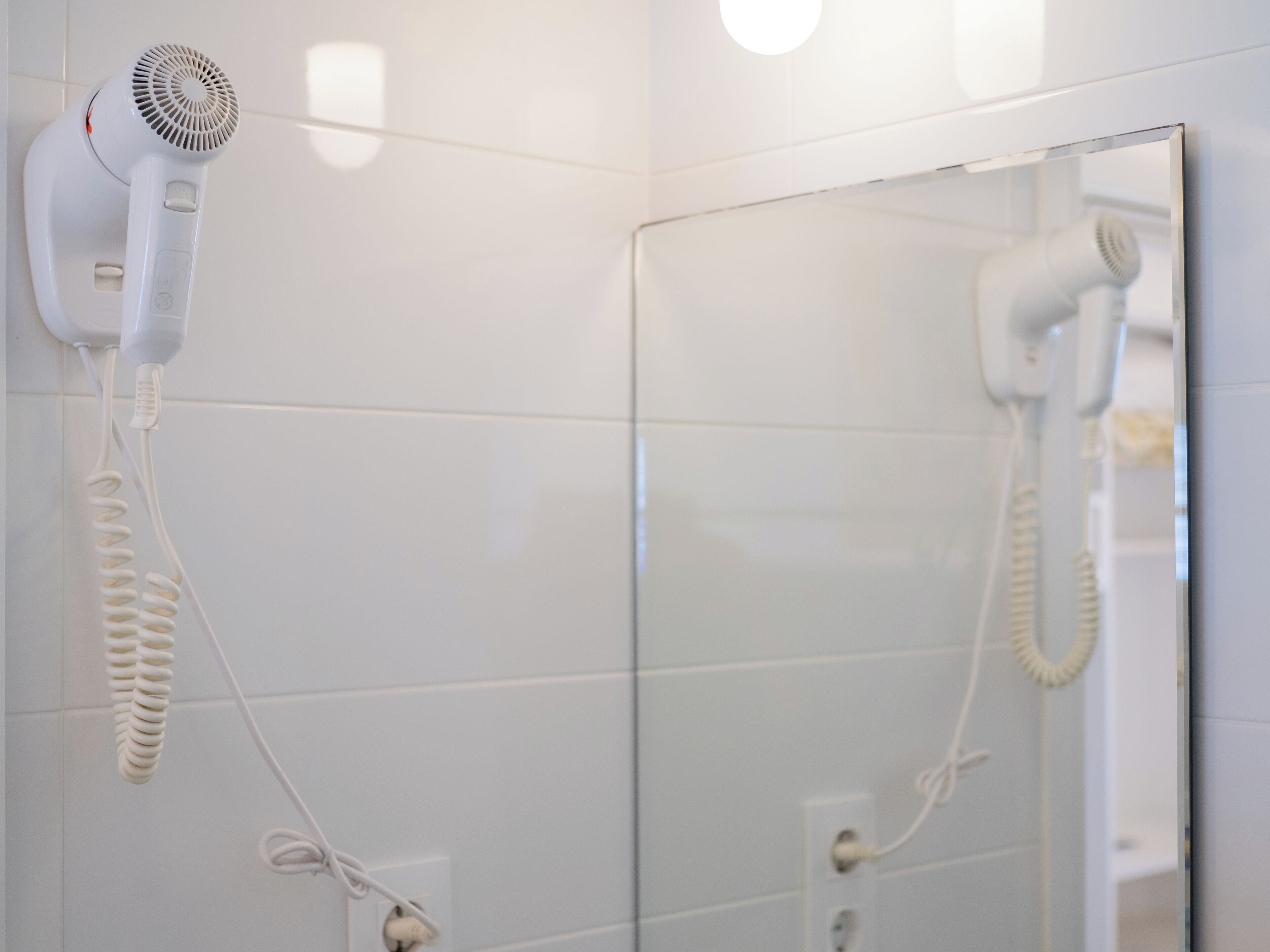 Un baño con un secador de pelo sujeto a la pared y un espejo.