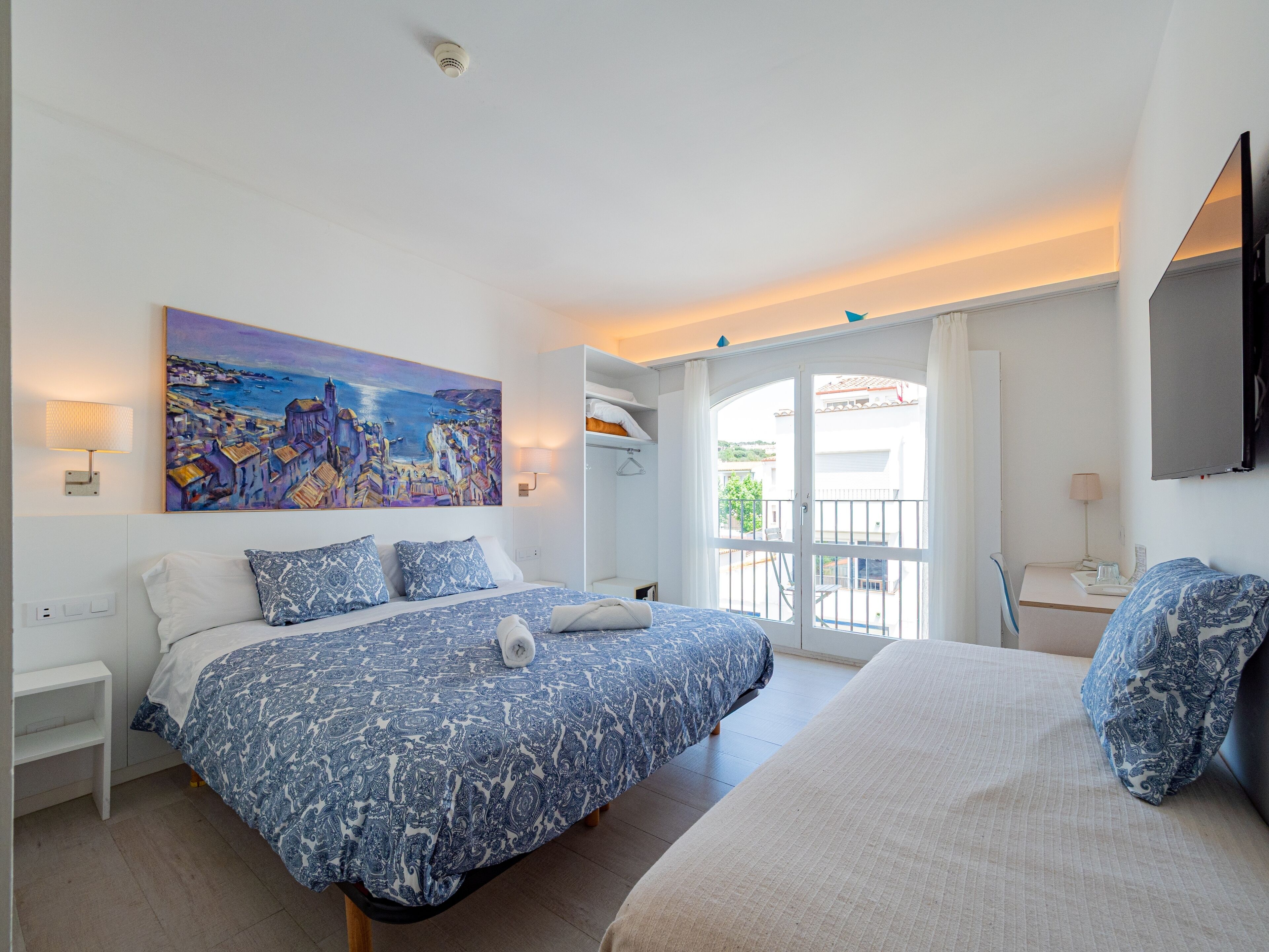 A hotel room with a bed, a desk, a chair, a TV, and a painting on the wall.