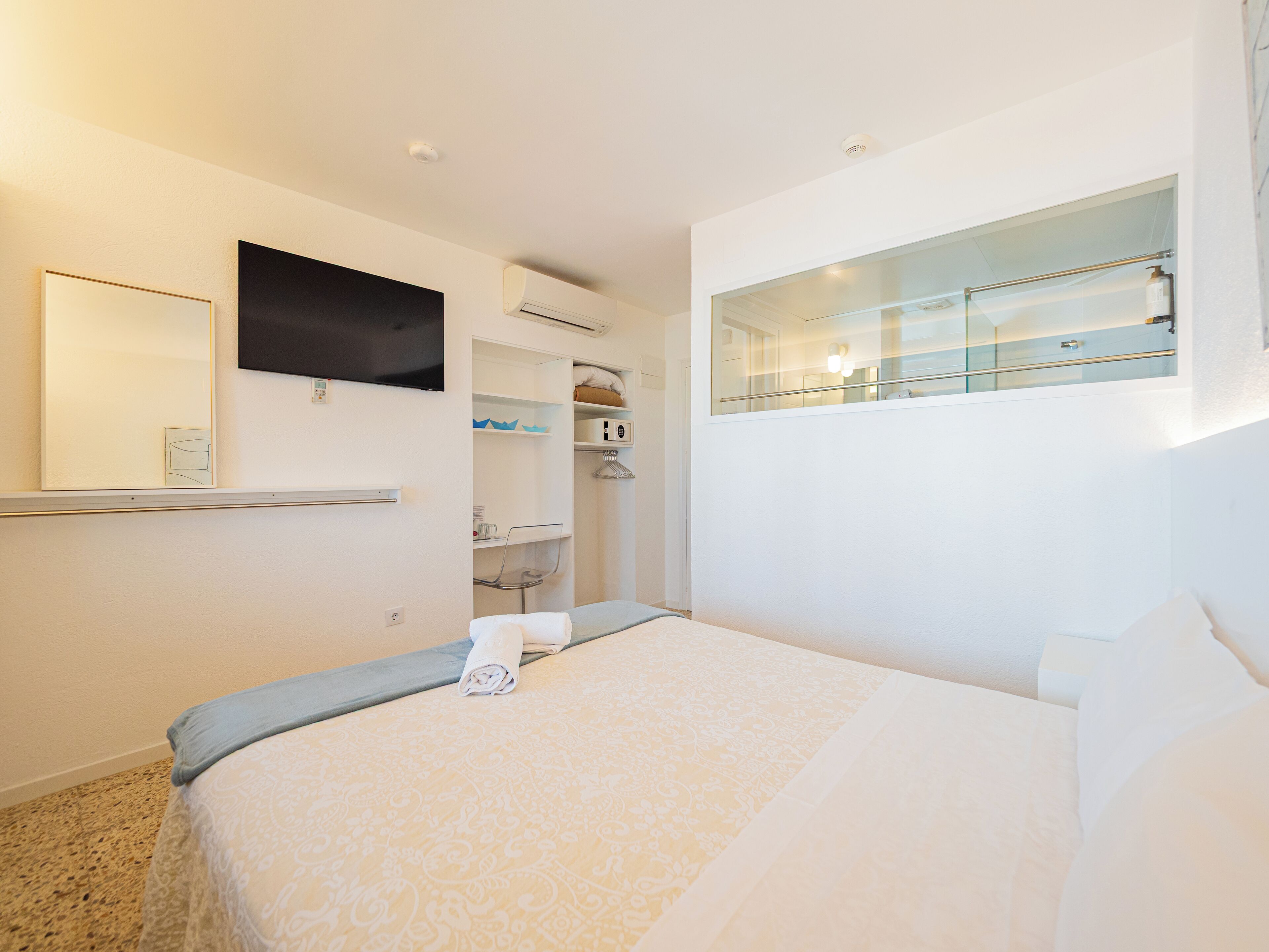 Une chambre d’hôtel équipée d’un lit, d’un téléviseur fixé au mur, d’une armoire intégrée et d’une cabine de douche en verre.