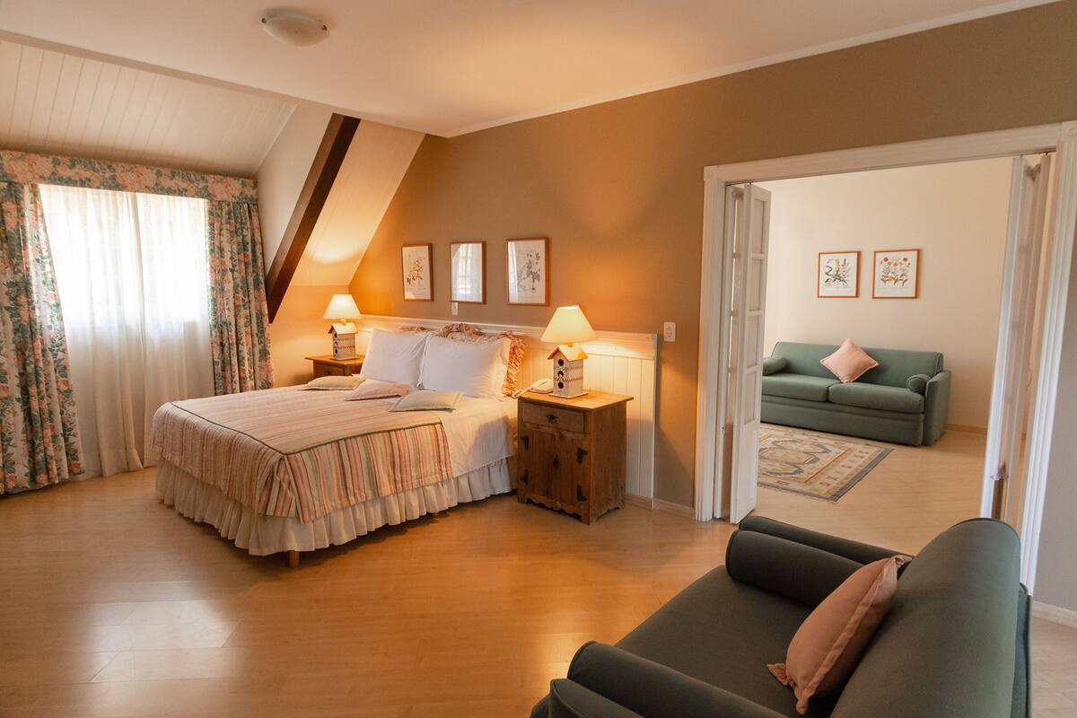 Ein Schlafzimmer mit einem Bett, Nachttischen, einem Beistelltisch, einem grünen Sofa und einer Tür zu einem anderen Raum.