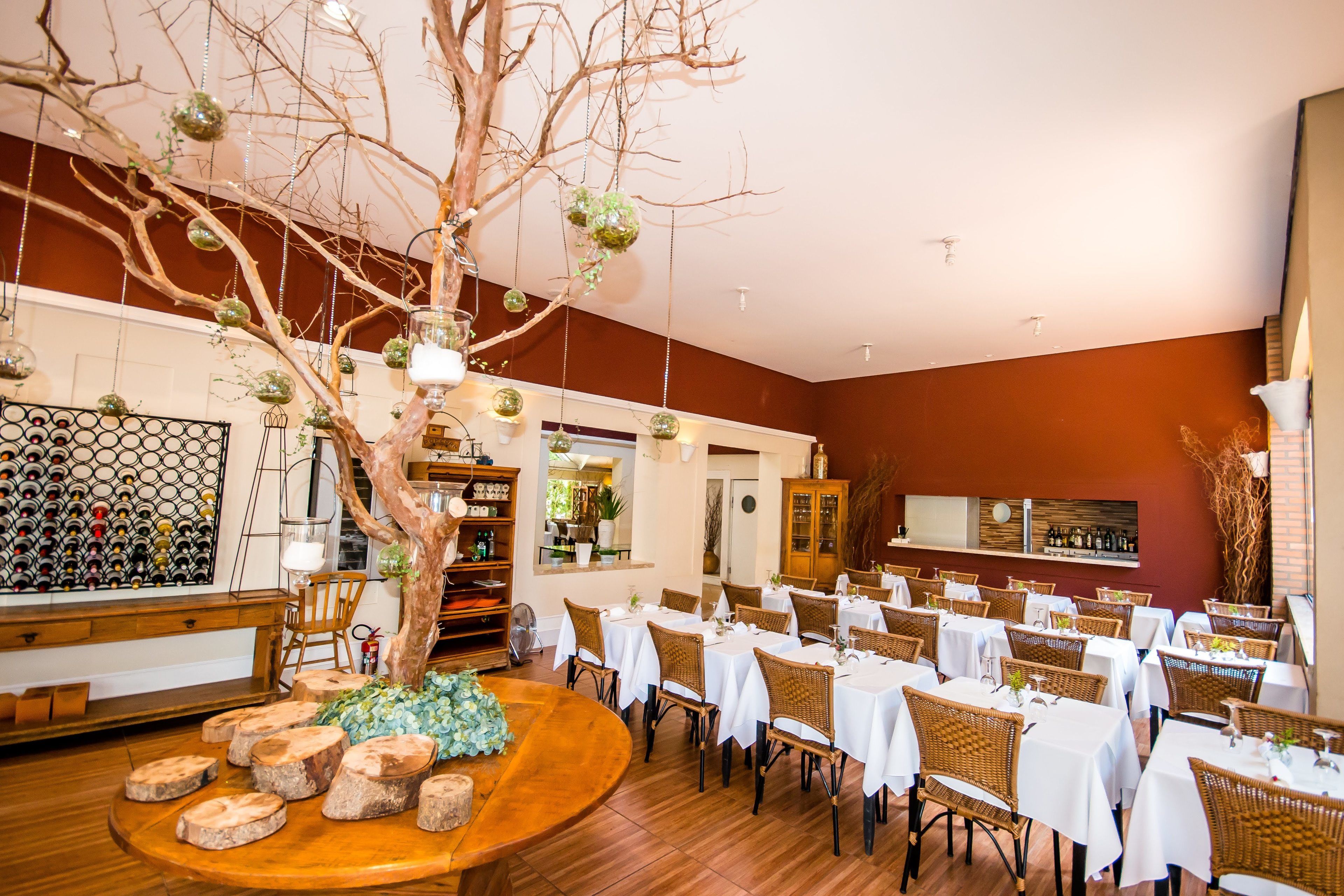 Un restaurante con mesas redondas, sillas de mimbre y un árbol central con adornos colgantes.
