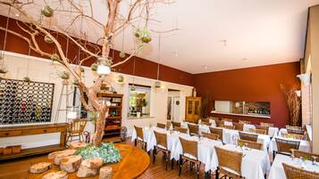 Un restaurante con mesas redondas, sillas de mimbre y un árbol central con adornos colgantes.