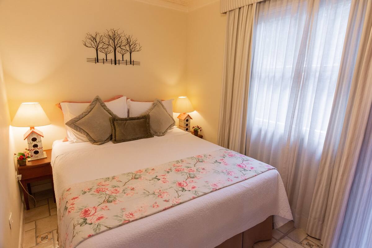 Ein ordentlich bezogenes Bett mit floraler Bettwäsche, zwei Nachttischlampen und einer an der Wand befestigten Baumdekoration.
