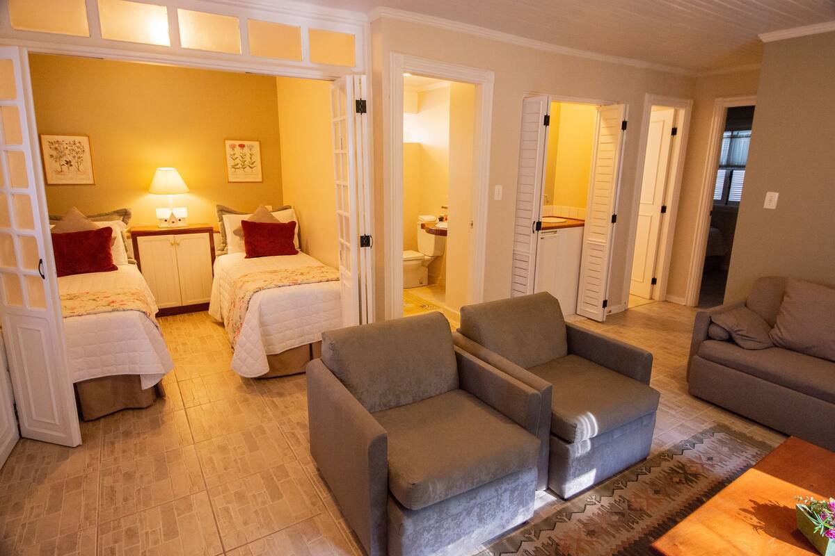 Ein Hotelzimmer mit zwei Betten, einem Schlafsofa und einem Sessel. Ein Badezimmer ist durch eine offene Tür sichtbar.