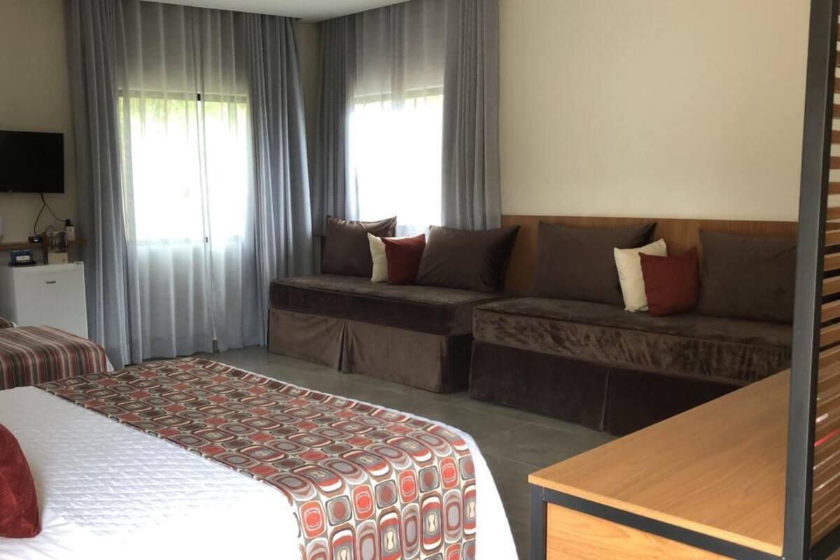 Ein Hotelzimmer mit zwei Betten, einer Schlafcouch, einem Fernseher und einem Schreibtisch.