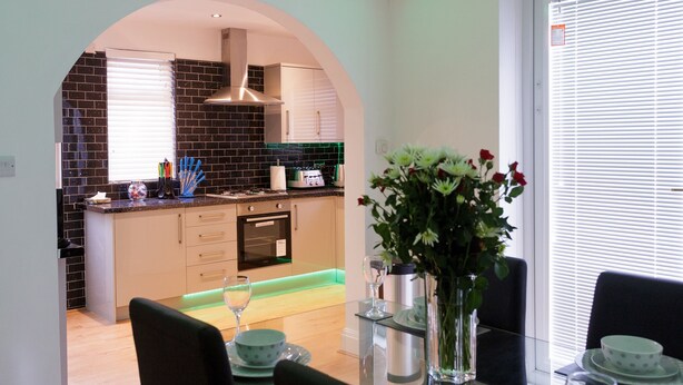 A modern kitchen with black tiled backsplash, stainless steel appliances, and a dining area with a glass table and chairs. - Sycamore House (Leeds)