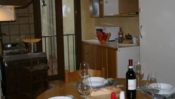 A dining area with a table set for two, a wine bottle, and a bowl of fruit on the counter. - Macci Art (Florence)