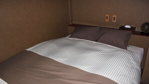 A neatly made bed with a striped bedspread and two pillows, a wooden nightstand with a lamp, and a textured wall. - Fuji Ginkei (Fujikawaguchiko)