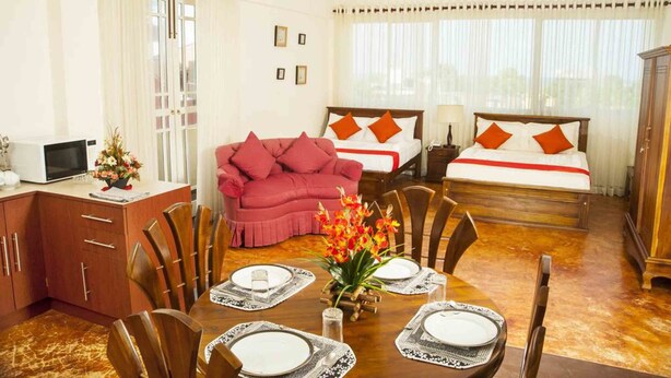 A hotel room with a dining area, a bed with two pillows, a red sofa, and a wooden cabinet. - The Prestige Court Residence (Mount Lavinia)