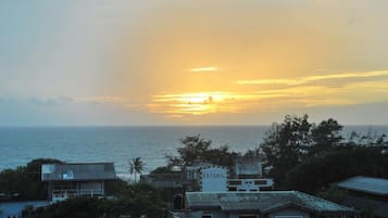 A coastal view with a sunset over the ocean, buildings with signage, and a clear sky.