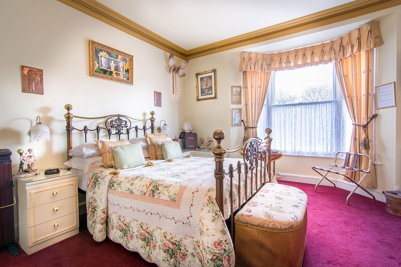 A bedroom with a wooden bed, floral bedding, a nightstand, a dresser, a window with curtains, and a chair.