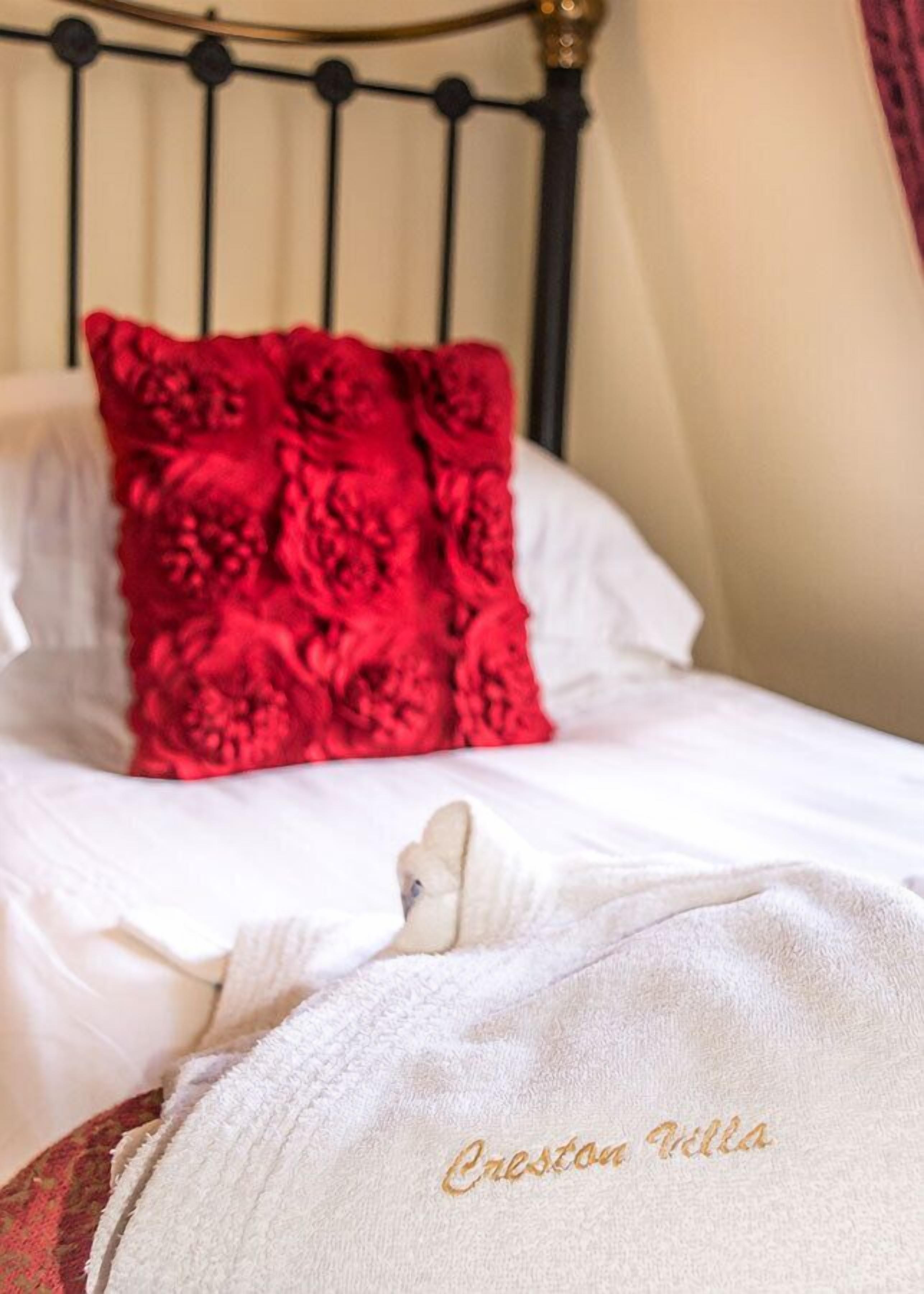 A neatly made bed with white bedding and a red floral pillow.
